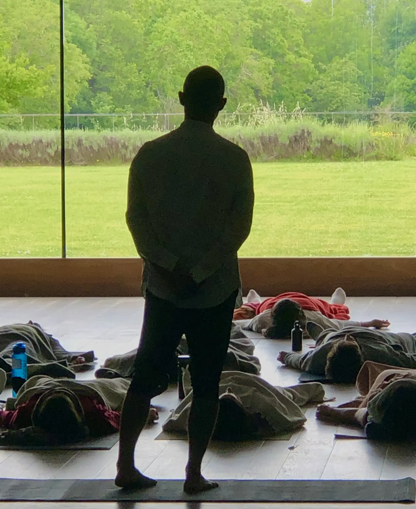 Andrei Ram standing, backlit, guiding a group practicing lying down
