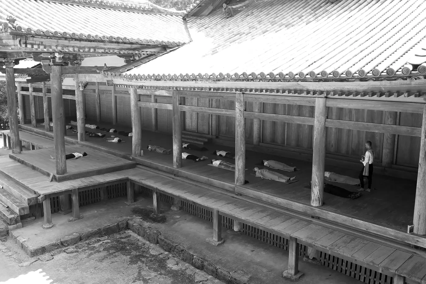 Un grupo practica acostado en la galería de madera de un templo japonés, con Andrei Ram de pie al fondo
